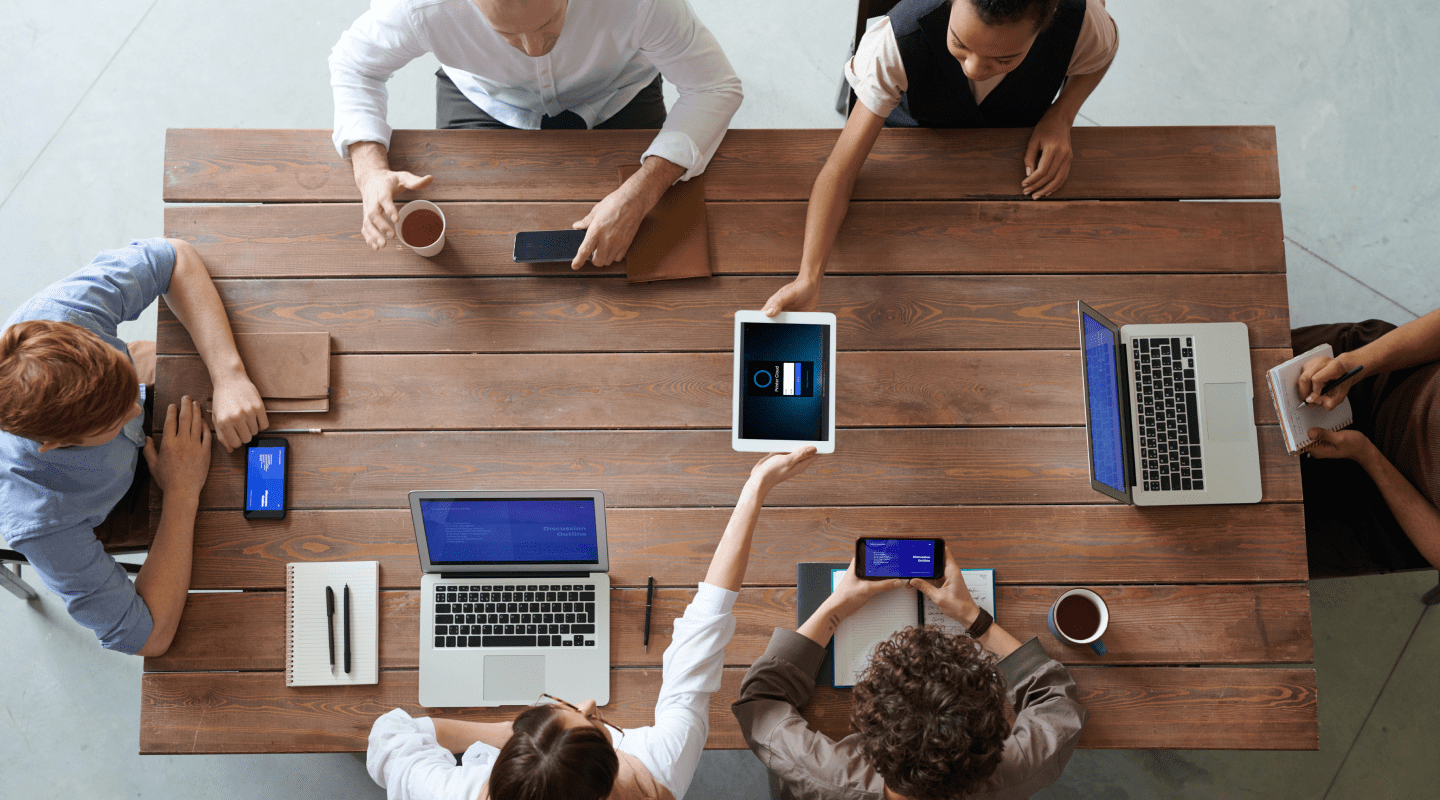 Um grupo de pessoas em reunião ao redor de uma mesa utilizando o Printer Cloud em seus dispositivos